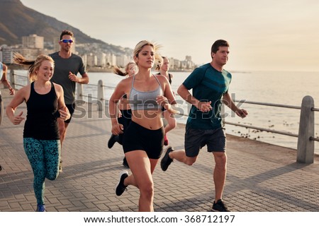 Confident young woman runs with friends. Group of young people doing running workout together in morning.