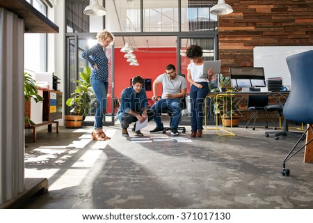 Mixed race group of creative people meeting in the office and discussing. Creative people looking at project plans laying on floor of modern workplace.