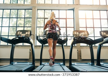 Horizontal shot of woman jogging on treadmill at health club. Female working out at a gym running on a treadmill.