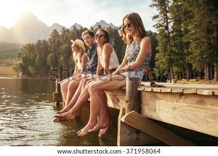 Portrait of group of young people sitting on the edge of a pier, outdoors in nature. Friends enjoying a day at the lake.