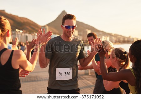 Group of young adults cheering and high fiving a male athlete crossing finish line. Sportsman giving high five to his team after finishing the race.