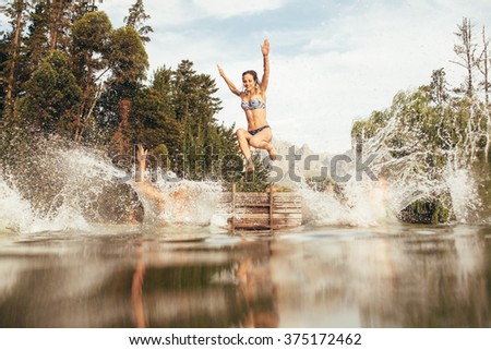 Portrait of young women jumping into a wilderness lake from the jetty. Young girl jumping from a pier at the lake