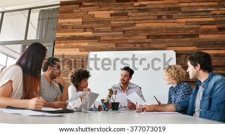 Group of business people having meeting in a board room in an office. Creative team sitting at the table discussing new strategy of their company.