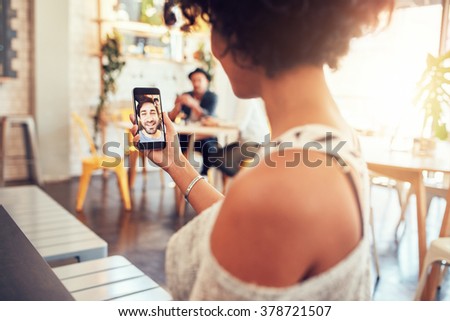 Man and woman talking to each other through a video call on a smartphone. Young woman having a videochat with man on mobile phone. Woman sitting at a cafe.