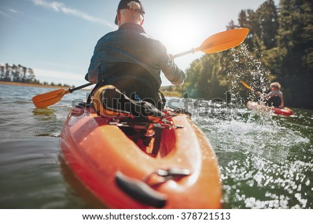 Rear view of man paddling kayak in lake with woman in background. Couple kayaking in lake on a sunny day.