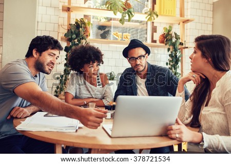 Portrait of young people sitting around a table in cafe with a laptop. Creative team discussing new business project at a coffee shop.