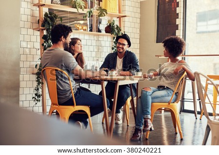 Young people sitting at a cafe table. Group of friends talking in a coffee shop.