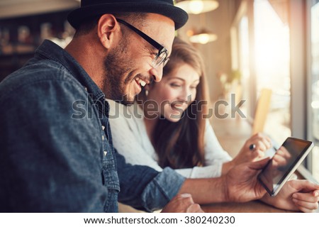 Close up portrait of happy young couple using a digital tablet together at a coffee shop. Young man and woman looking at touch screen computer and smiling.