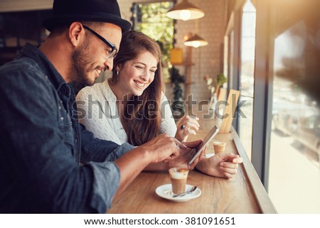 Happy couple in a coffee shop surfing internet on digital tablet. Young man and woman in a restaurant looking at touch screen computer.