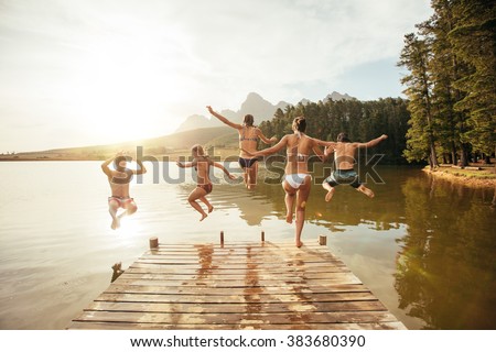 Portrait of young friends jumping into the water from a jetty. Young people having fun at the lake on a summer day.