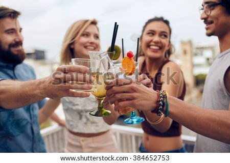 Friends having fun and drinking cocktails outdoor on a rooftop get together. Group of friends hanging out and toasting drinks outdoors. Focus on glasses.