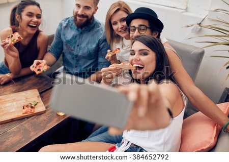 Group of multiracial young people taking a selfie while eating pizza. Young woman eating pizza her friends sitting around during a party.