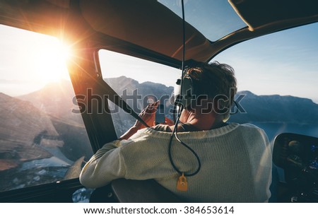Rear view of female tourist on helicopter tour taking pictures while flying over mountains on a sunny day.