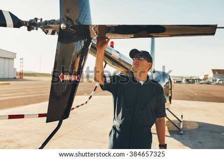 Male pilot in uniform examining helicopter tail wing. Pre flight inspection by pilot at the airport.