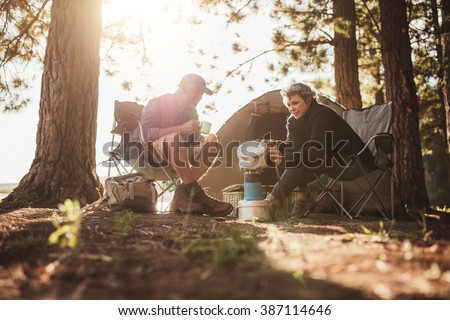 Senior couple cooking and making food outdoors on a camping trip. Mature man and woman sitting outside the tent on a summer day at campsite.