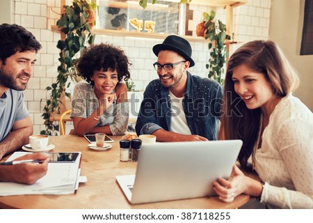 Group of friends hanging out in a coffee shop with a laptop amongst them. Happy young people sitting at restaurant using laptop computer.