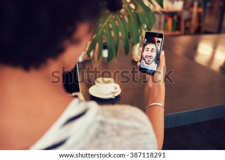 Young an and woman talking to each other through a video call on a smartphone. Young woman having a videochat with man on mobile phone. Woman sitting at a coffee shop.