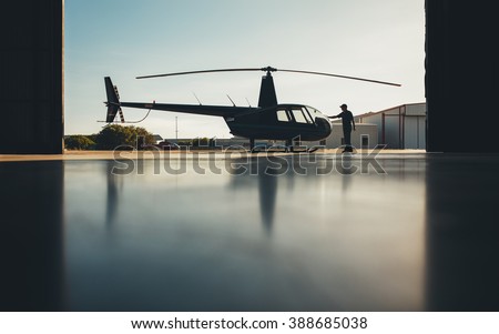 Silhouette of helicopter in the hangar with a pilot. Pilot doing preflight inspection of a helicopter.