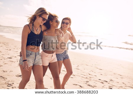 Portrait of three young female friends walking on the sea shore. Multiracial young women strolling along a beach on a summer day.