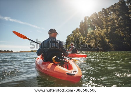 Outdoor shot of mature man canoeing in the lake with woman in background. Couple kayaking in the lake on a sunny day.