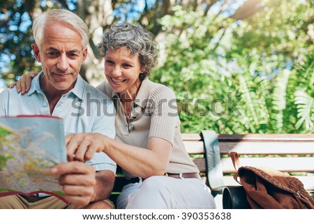 Portrait of happy man and woman reading map while sitting on a park bench. Senior couple on vacation using city map.