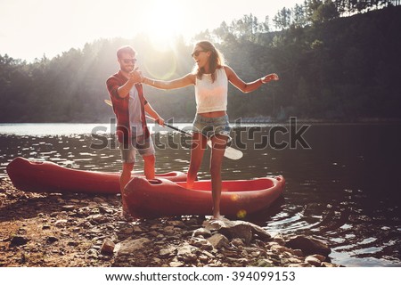 Young man helping woman to step out of a kayak. Couple after kayaking in the lake on a sunny day.