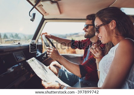 Side view of young couple using a map on a roadtrip for directions. Young man and woman reading a map while sitting in a car.