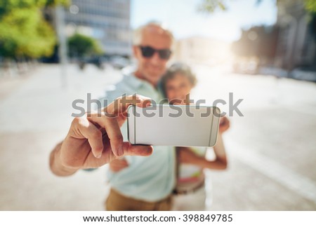 Happy senior couple embracing and taking a self portrait on mobile phone outdoors. Tourist taking selfie, focus on mobile phone..