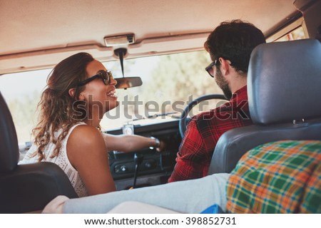 Rear view shot of a young couple enjoying a road trip. Happy young woman with her boyfriend driving a SUV car.