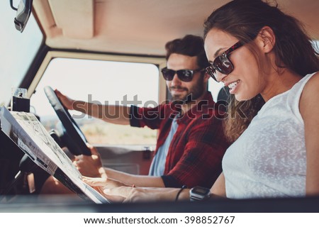 Side view of young couple reading a map for directions. Young man and woman in the car going on roadtrip.