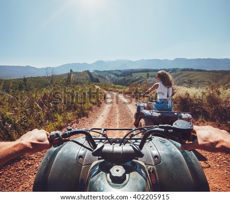 Young people on quad bikes on a countryside trail. View from a quad bike with woman driving an ATV in front on a sunny day.