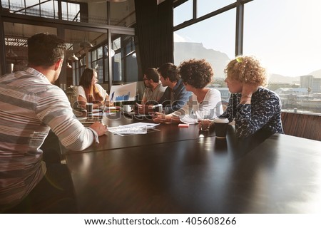 Young woman giving a presentation to colleagues in office. Mixed race team of creative professionals in a meeting at office.
