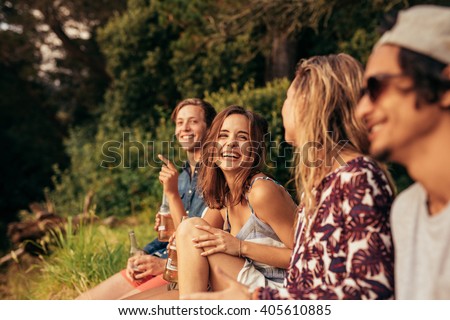Portrait of cheerful young friends hanging out with beers. Group of friends sitting outdoors and having fun.