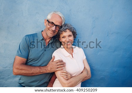Portrait of smiling mature couple standing together against blue background. Happy middle aged man and woman against a wall.