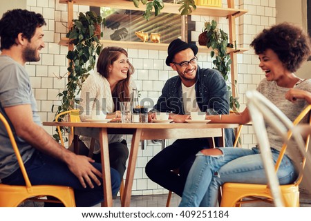 Young people having a great time in cafe. Friends smiling and sitting in a coffee shop, drinking coffee and enjoying together.