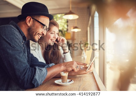 Smiling young couple in a coffee shop using touch screen computer. Young man and woman in a restaurant looking at digital tablet.