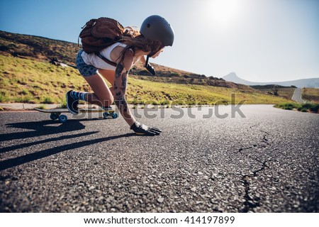 Young woman riding on her skateboard. Female skater practicing skating on country road.