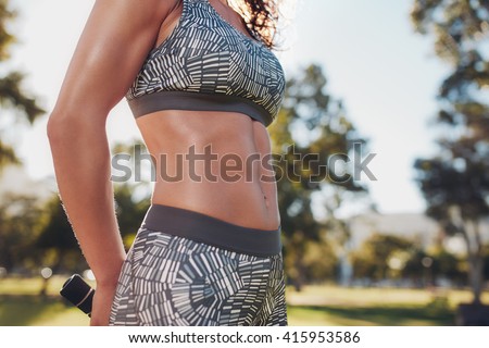 Midsection shot of fit woman in sportswear outdoors at the park. Very fit body with strong six-pack abs.