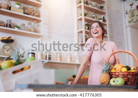 Portrait of beautiful young woman standing at a juice bar counter and looking away smiling. Successful female juice bar owner.