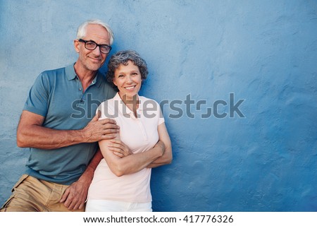 Portrait of happy senior man and woman together against blue background. Middle aged couple looking at camera and smiling with copy space on blue wall.
