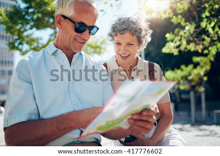 Elderly couple sitting outdoors and using city map. Happy retired couple looking for a destination on a city map.