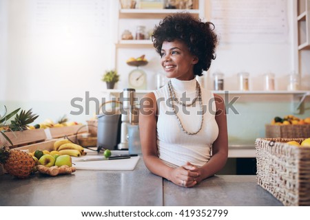 Portrait of beautiful young woman working at juice bar, she is standing behind counter looking away and smiling.