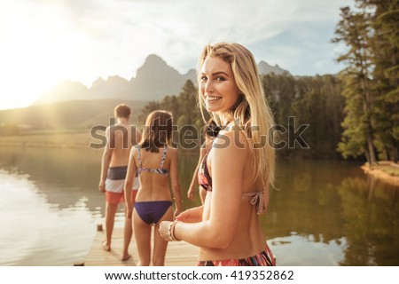 Portrait of an beautiful young girl with friends on a jetty on a lake. Young people having fun on a summer day at the lake.