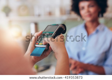 Young woman paying by credit card at juice bar. Focus on woman hands entering security pin in credit card reader.