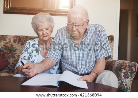 Portrait of a retired couple looking over documents while sitting at home. Senior caucasian man and woman sitting on sofa and signing some paperwork.