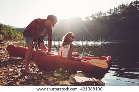 Young man pushes a canoe in the water while a woman sitting on the canoe. Couple going for kayaking in lake on a summer day.