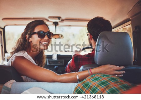 Happy young woman looking back with man driving car. Couple in a car going on roadtrip.