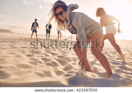 Young woman running race on the beach with friends. Group of young people playing games on sandy beach on a summer day.