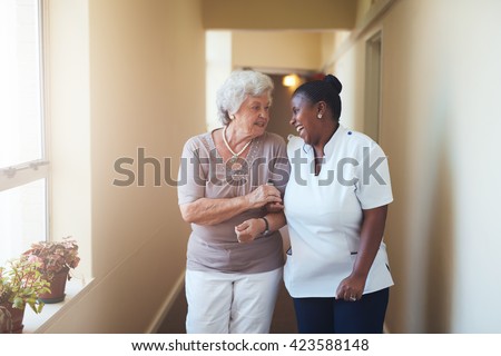 Portrait of happy female caregiver and senior woman walking together at home. Professional caregiver taking care of elderly woman.