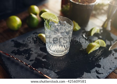 Close up of freshly made gin and tonic drink with lemon slices and spoon on a black board.